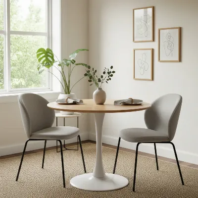 A modern round dining table with a pedestal base, seating two to three people in a bright, minimalist small apartment dining area.